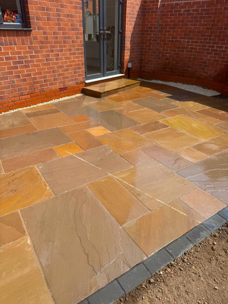 Freshly laid mixed-tone Indian sandstone patio with charcoal block paving edging outside bifold doors — Shrewsbury