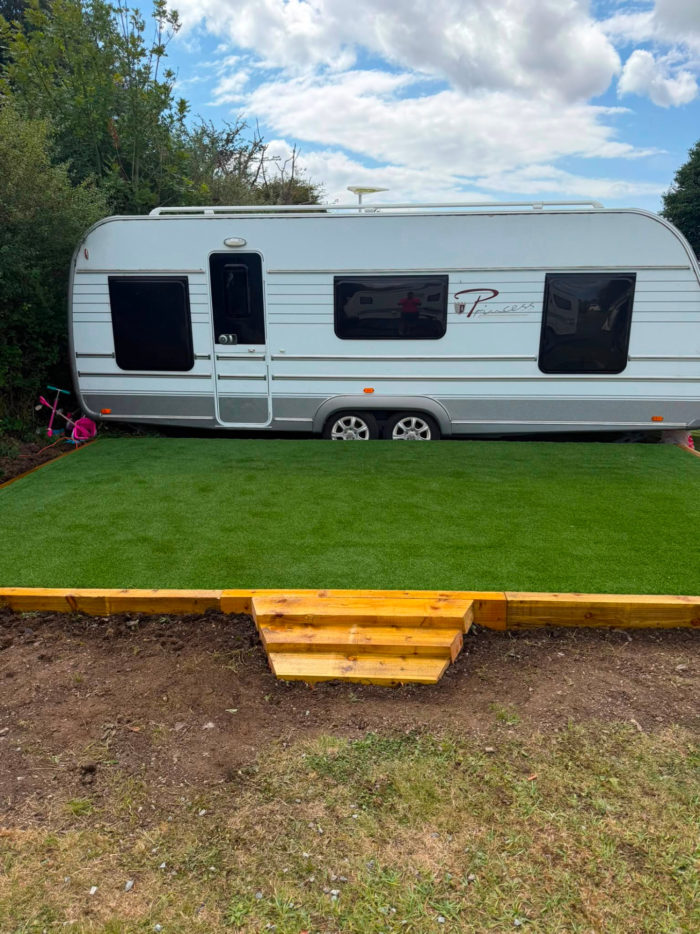 Artificial grass pitch with sleeper surround and built-in timber step in front of a caravan